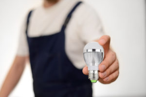 Worker in overall holding modern LED bulb in his hand over white background